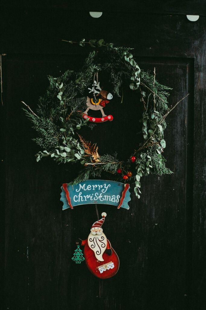 Close-up of a rustic Christmas wreath on a dark door with seasonal decorations.
