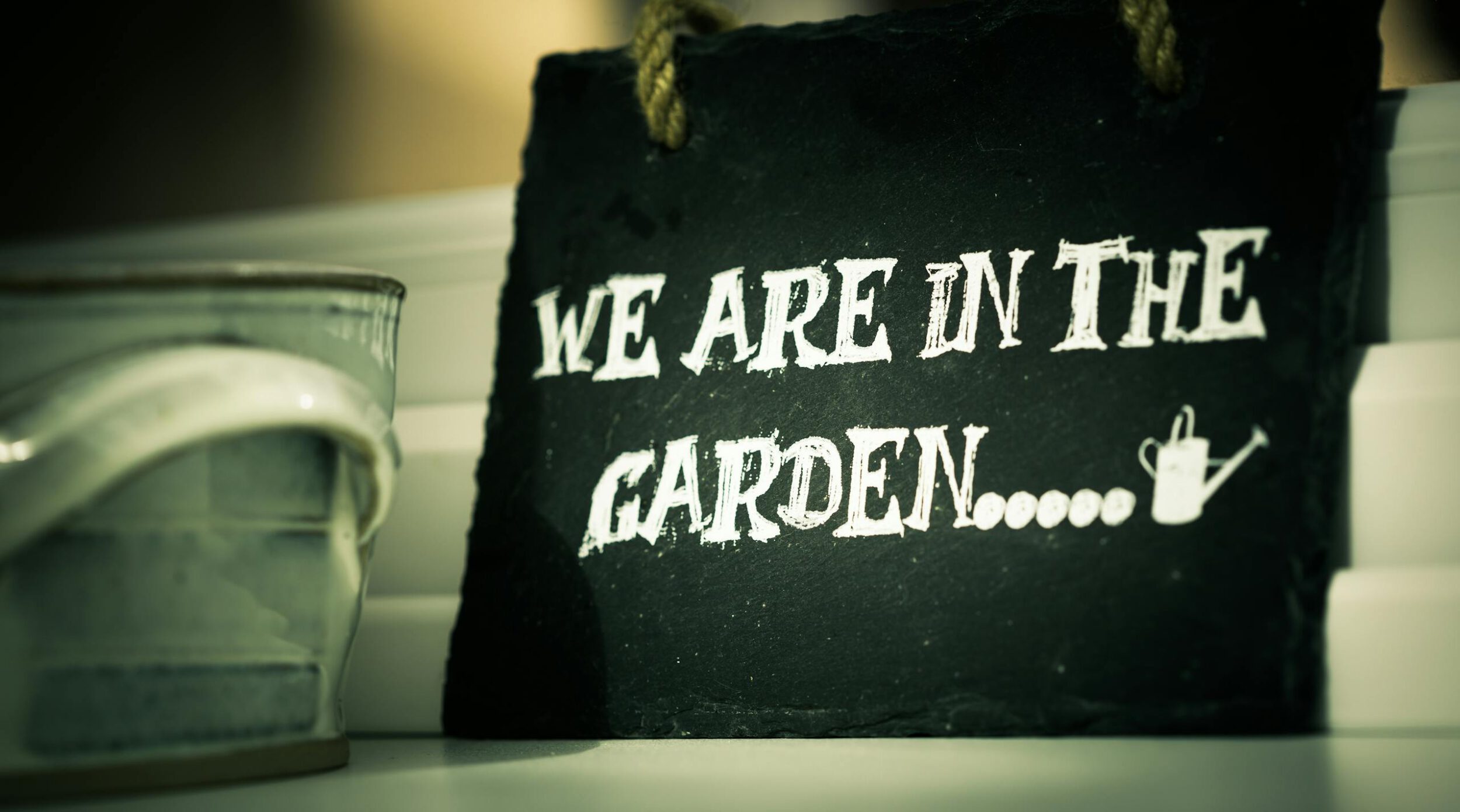 Close-up of a rustic slate sign reading "We Are In The Garden."